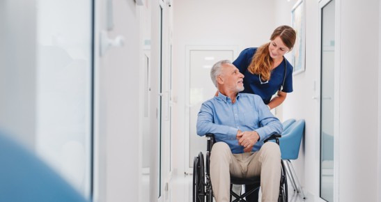 Praxisangestellte schiebt Mann in einem Rollstuhl